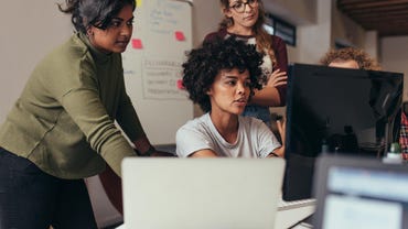 Multi-ethnic young women working together standing and sitting around a computer