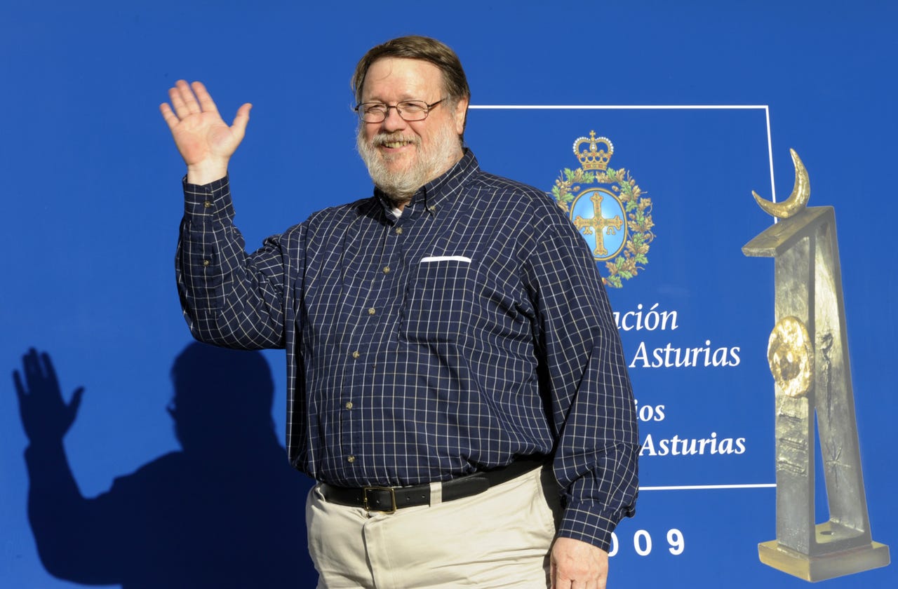 Programmer Ray Tomlinson smiles and waves in front of a backdrop
