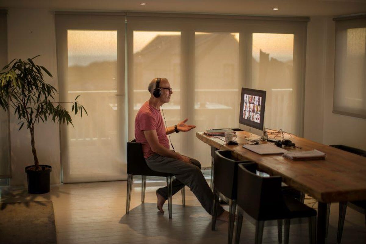 Middle aged man working form home in a kitchen, wearing headphones and speaking on a video call