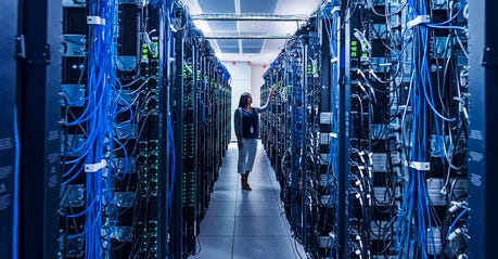 A woman stands between rows of servers.