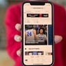 Young woman in a red sweater holding up the NCAA March Madness Live app on an iPhone.