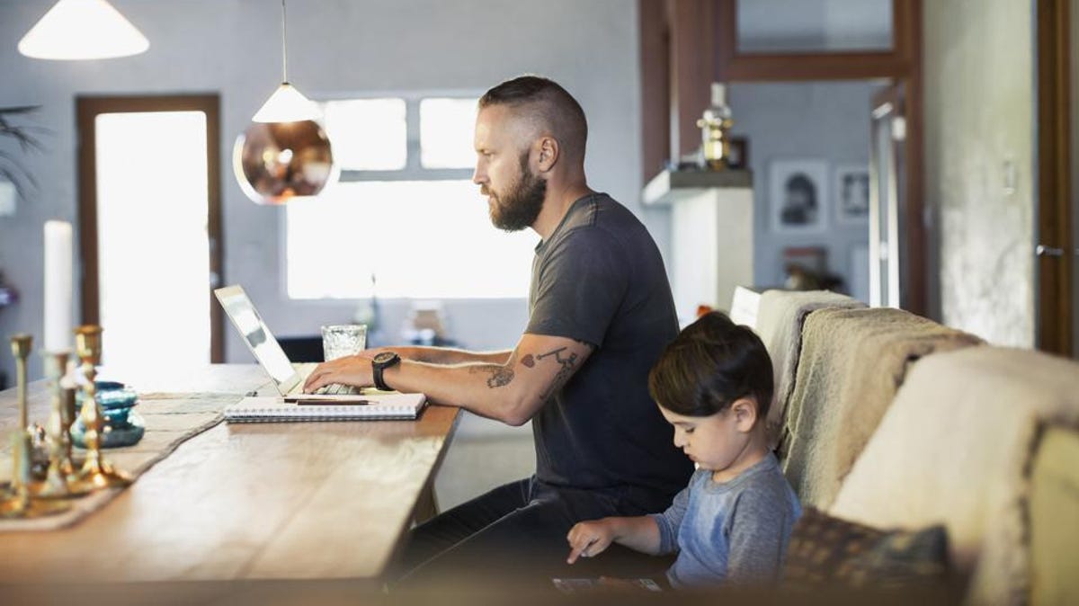 a young father working on a laptop next to his young son