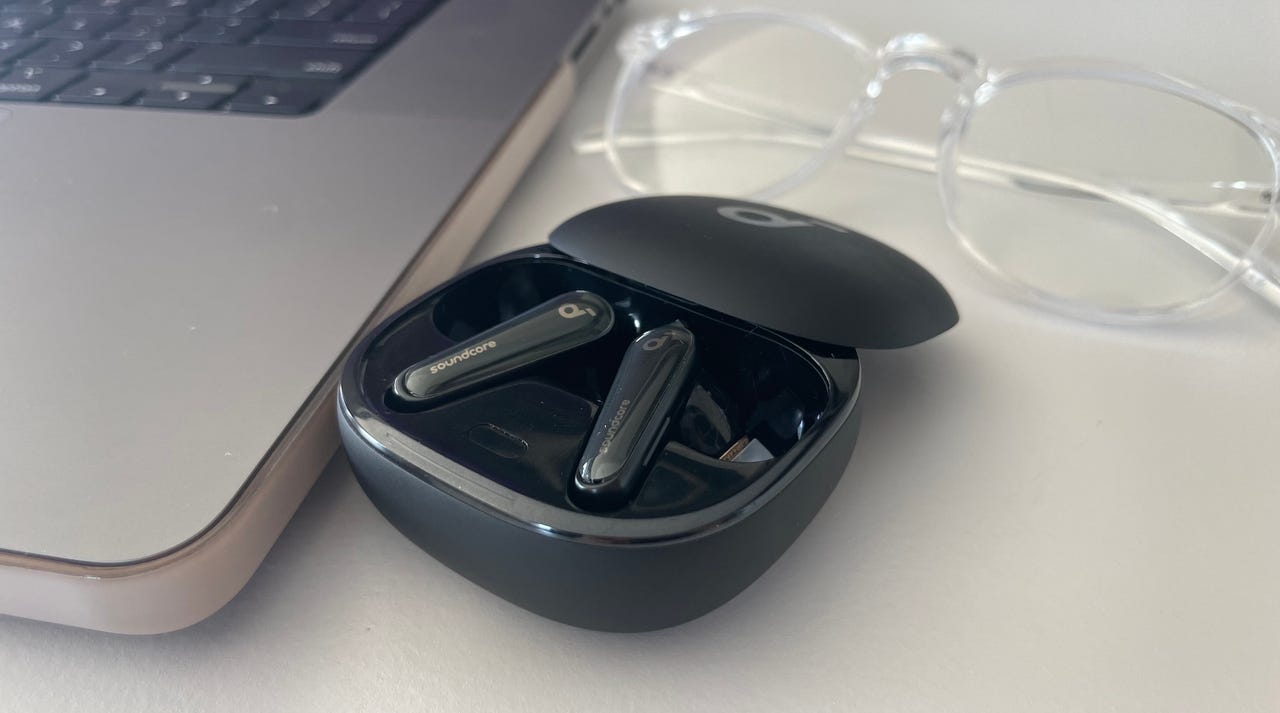 Liberty 4 earbuds on a desk next to a laptop and glasses