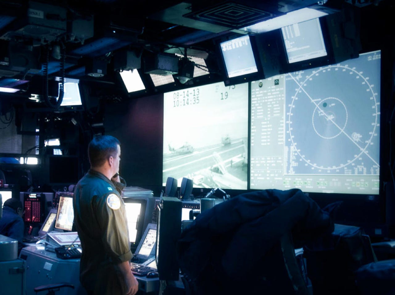 airforce member looking at a large screen in a dark command room.