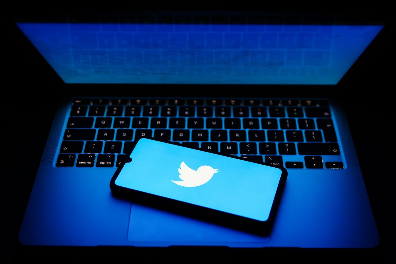 Twitter logo on phone, resting on laptop