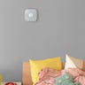 A Google Nest Protect mounted on a grey wall above a child's bed