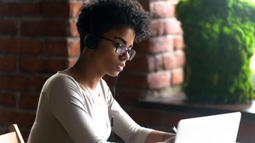 Focused African American woman wearing headphones using laptop