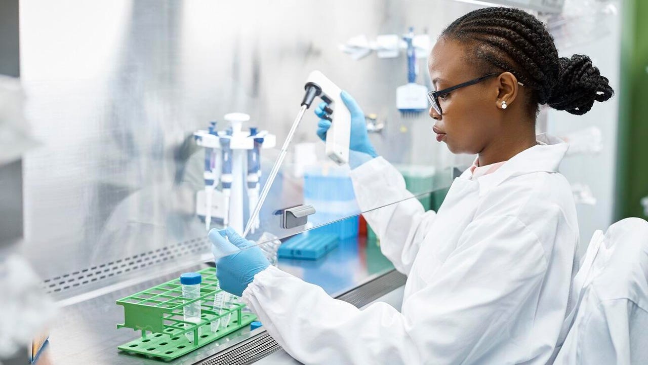 A Black, female scientist pipetting a sample into test tube.