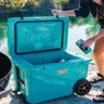 Person opening teal blue cooler outside next to a river