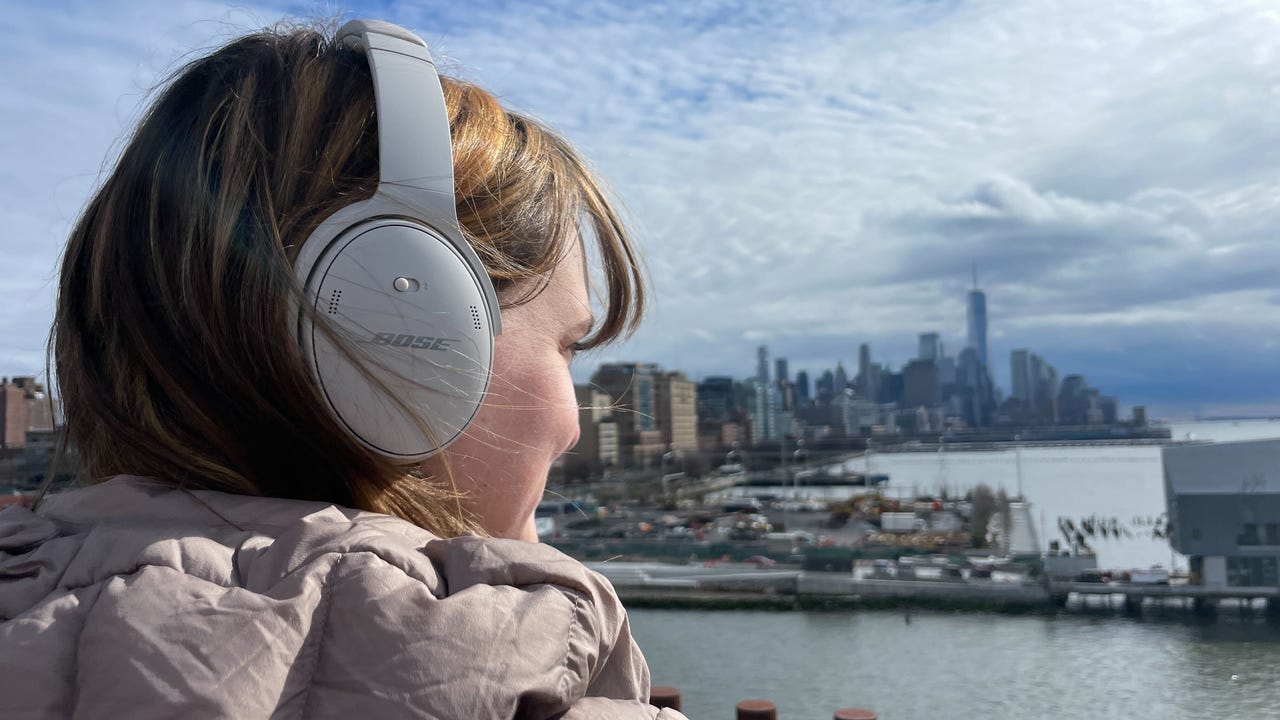 Woman with brown hair wearing Bose Quiet Comfort 45 headphones looking over the New York skyline.