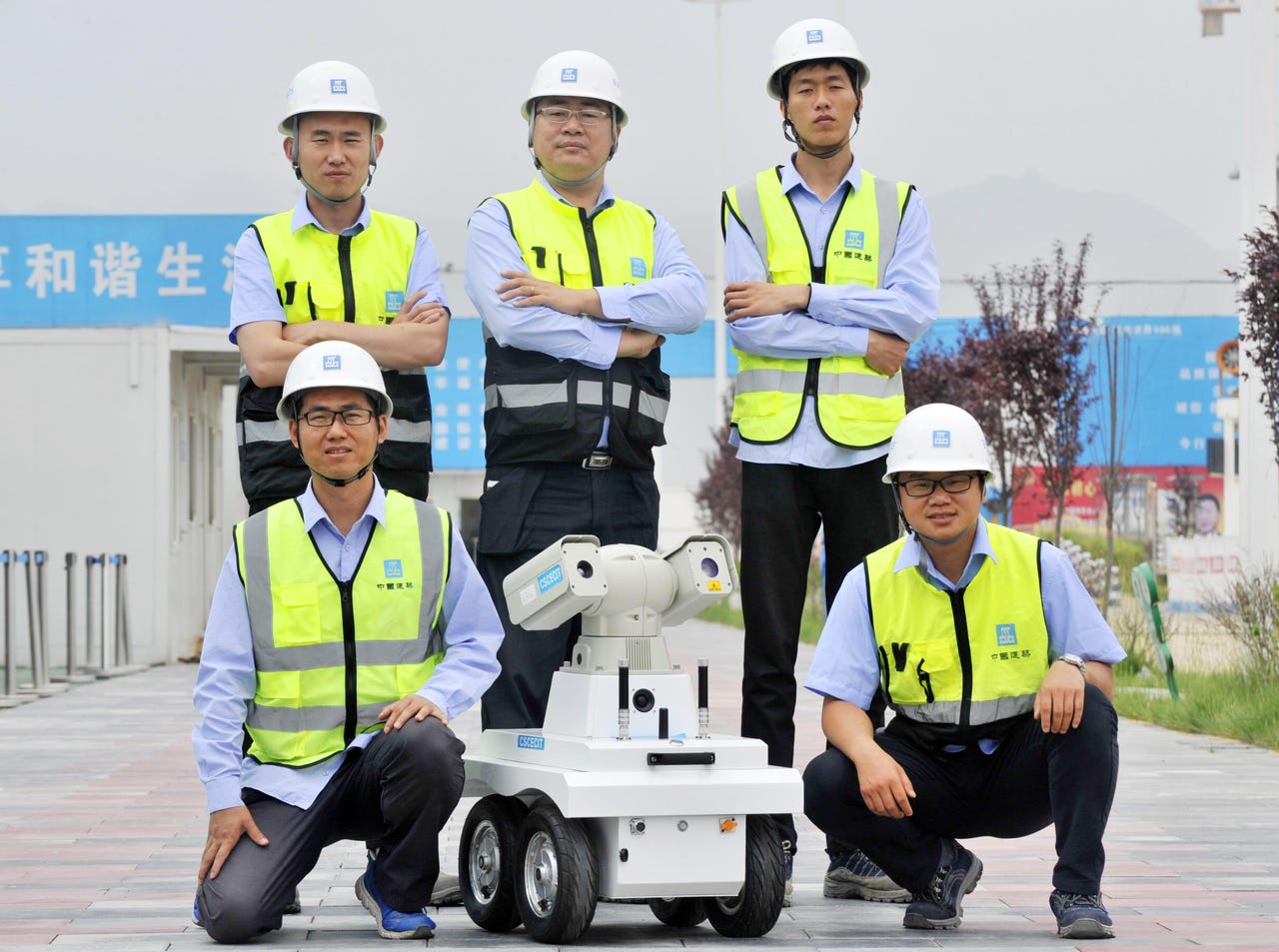 Five people in safety gear posed for a team photo with a wheeled inspection robot.
