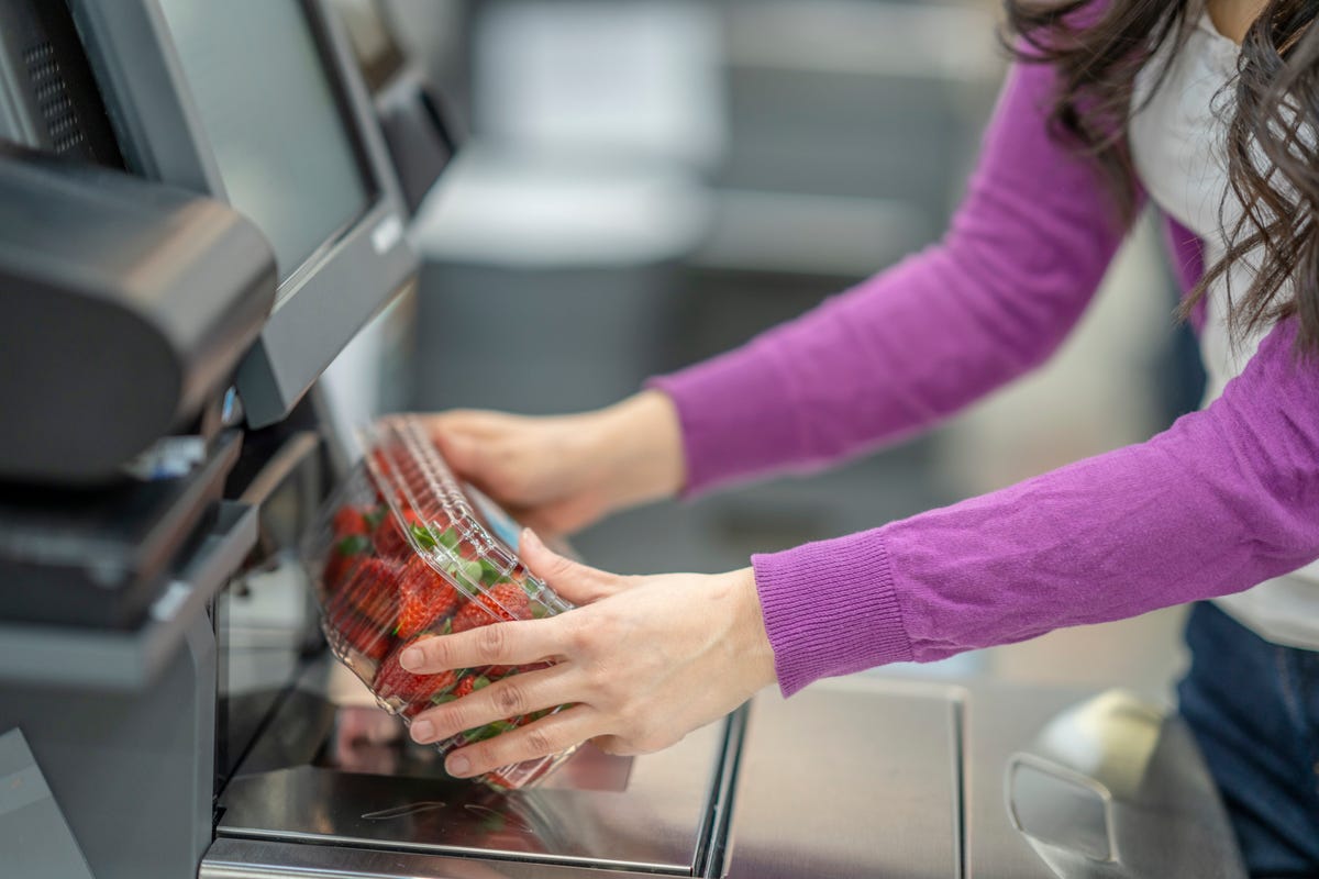 A woman scans a container of strawberries at self checkout.