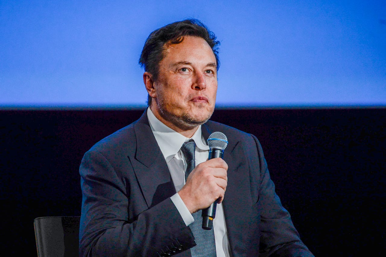 Elon Musk sitting down holding a microphone