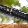 Image of black Fenix PD36R Flashlight with a forest background.