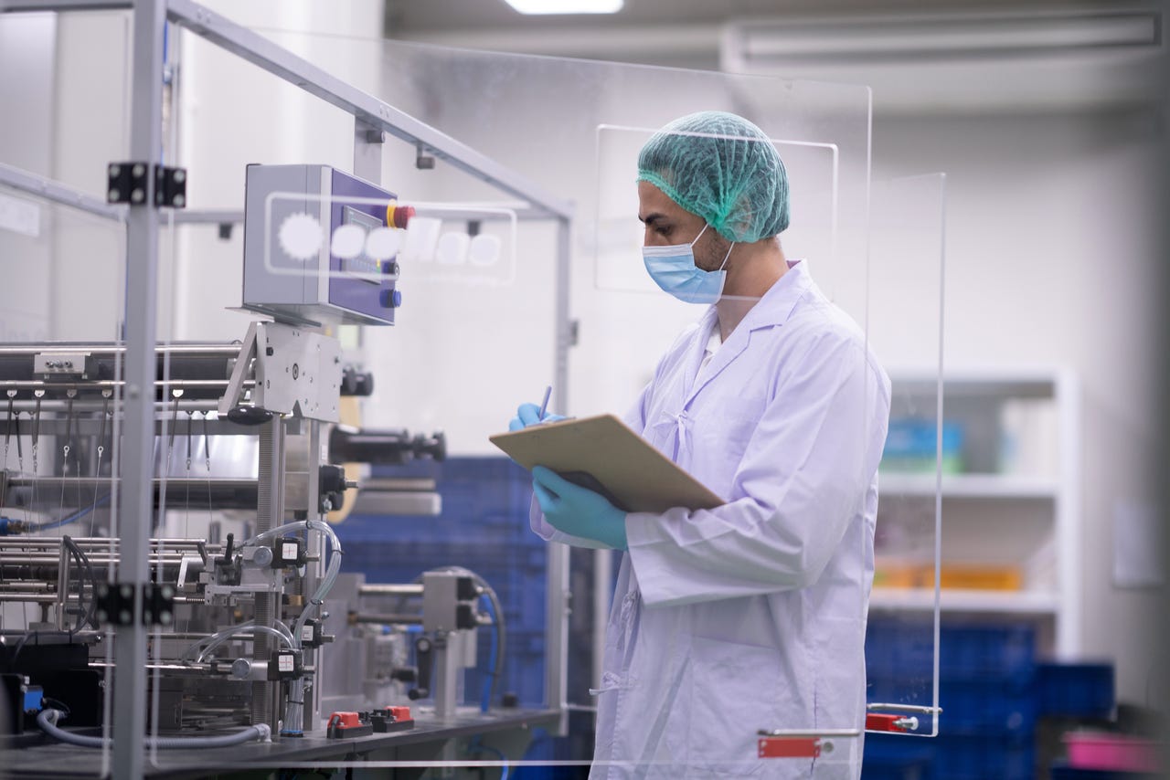 Técnico de laboratorio inspeccionando la fabricación farmacéutica en una sala controlada por contaminantes