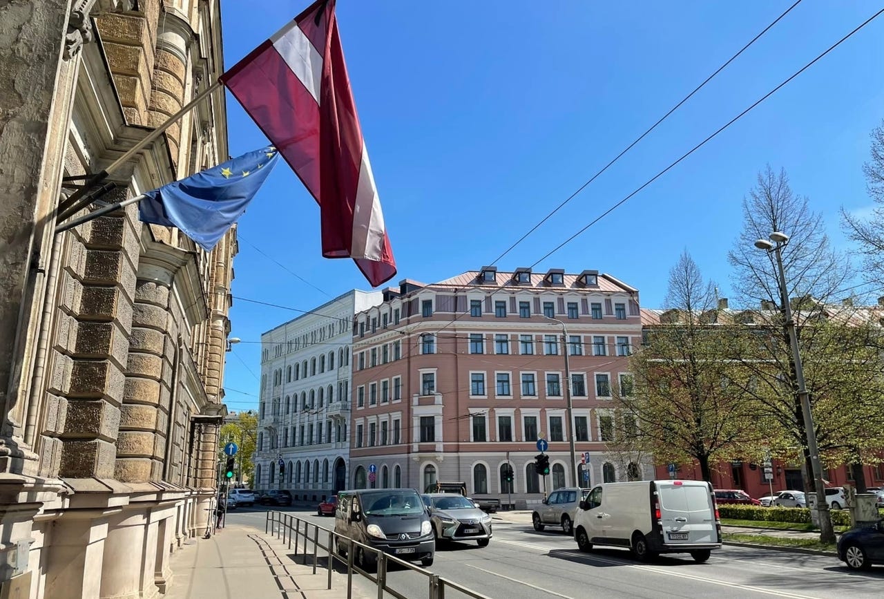 A sunny street in Latvia with the Latvian flag hanging from a building