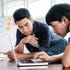 two young men with dark hair looking at a laptop
