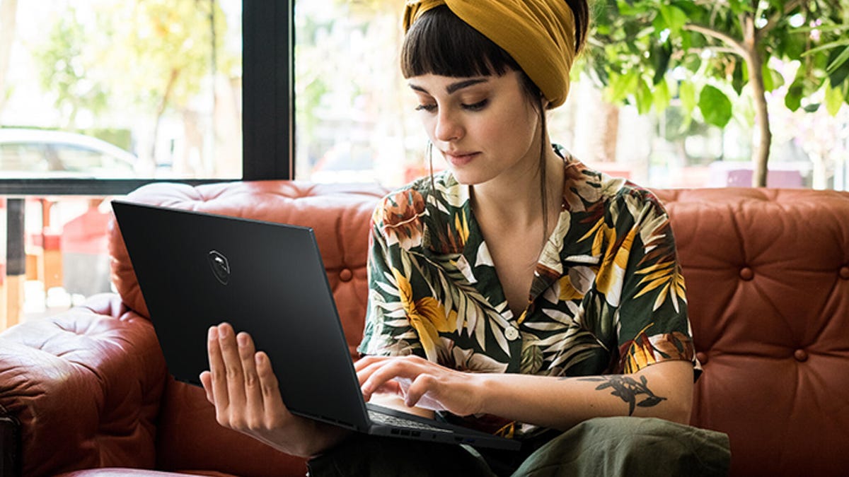 A woman in a floral shirt and yellow headband using an MSI Creator 15 laptop on a brown leather couch.