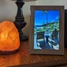A digital photo frame with a vacation photo on its screen next to a salt lamp on a living room side table