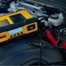 A DeWalt 30A car battery charger resting on the engine of a Chevy Trailblazer and connected to the battery