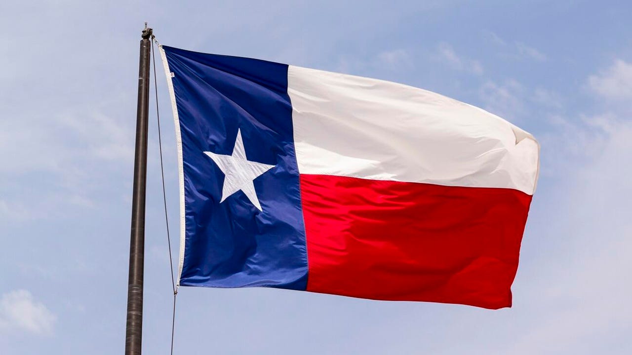 The flag of the state of Texas flies in front of a blue sky.