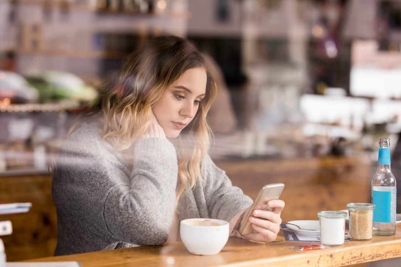 Image of a person scrolling on a smartphone at a coffee shop.