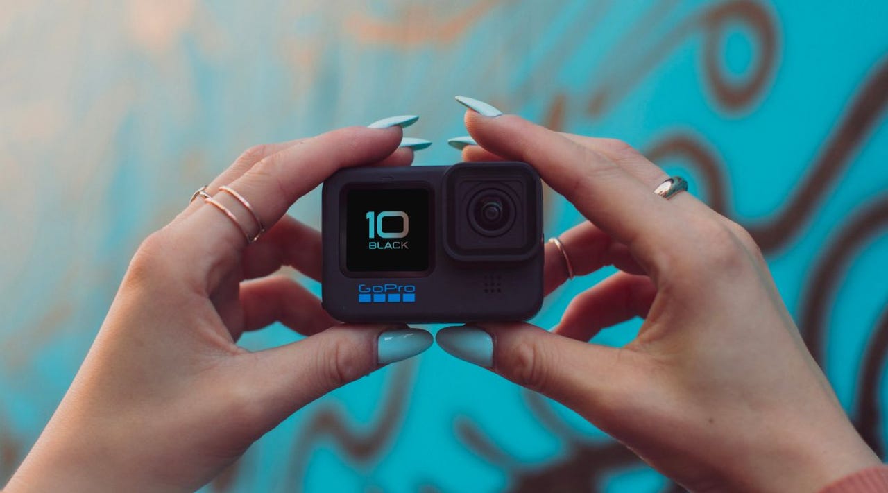 Hands holding up a GoPro HERO10 Black in front of graffiti