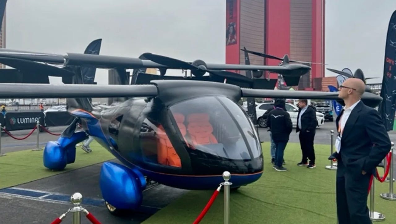 Helicopter looking vehicle that has a black body and blue wheels on a turf launch pad.