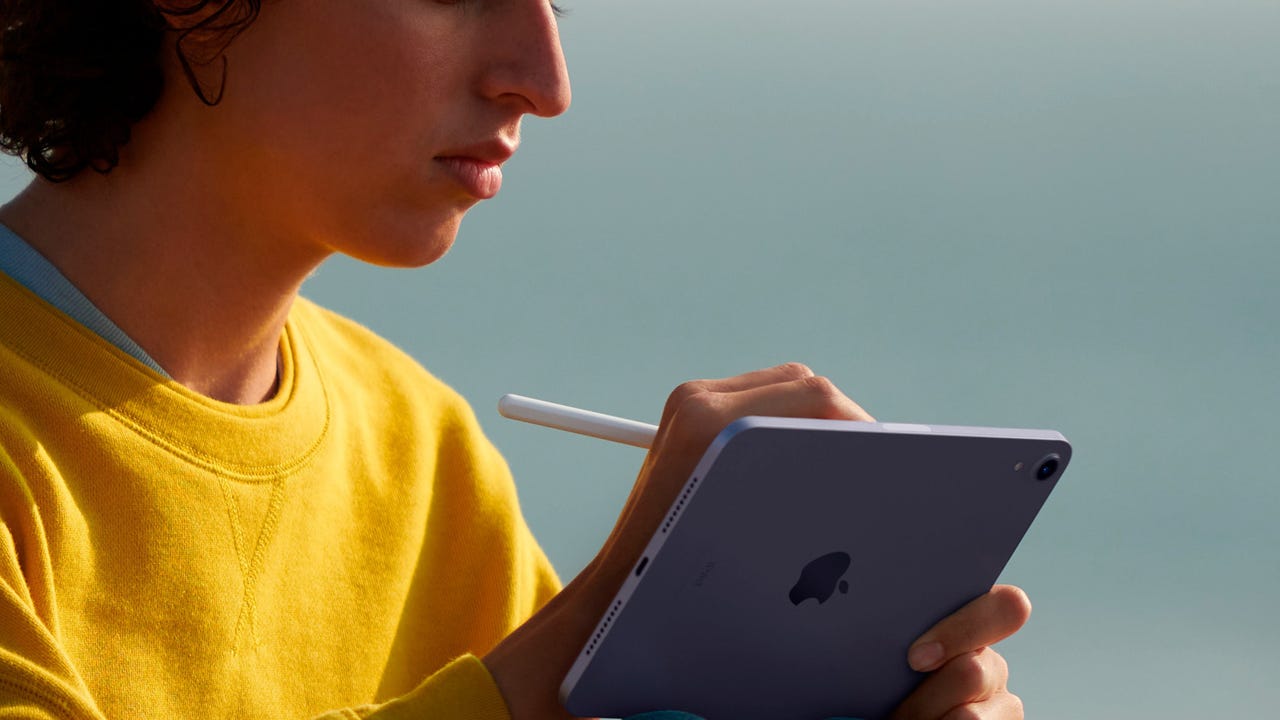 A young man in a yellow sweatshirt using an iPad Mini outside.