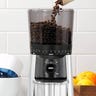 Coffee beans being poured into a coffee grinder on a kitchen counter