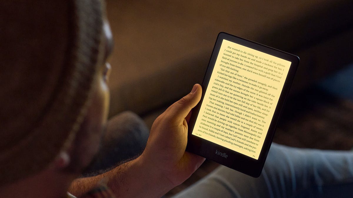 Close-up of a man in a knit beanie using the Amazon Kindle Paperwhite to read a book.