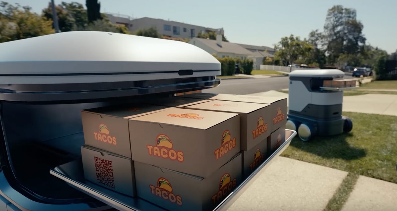 A delivery bot outdoors holding a tray of boxes labeled Tacos