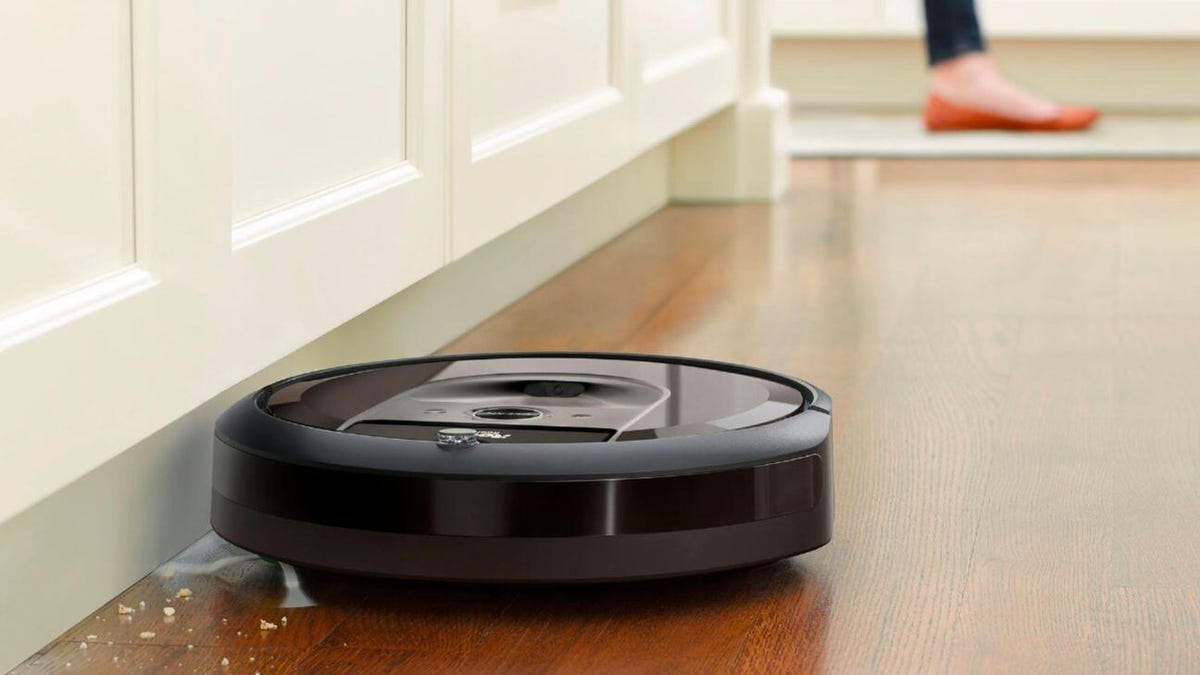 Black round Roomba vacuuming debris on a wooden floor