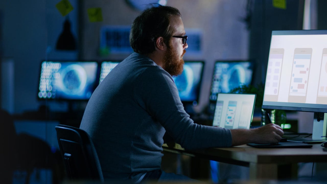 Man working surrounded by monitors in the dark