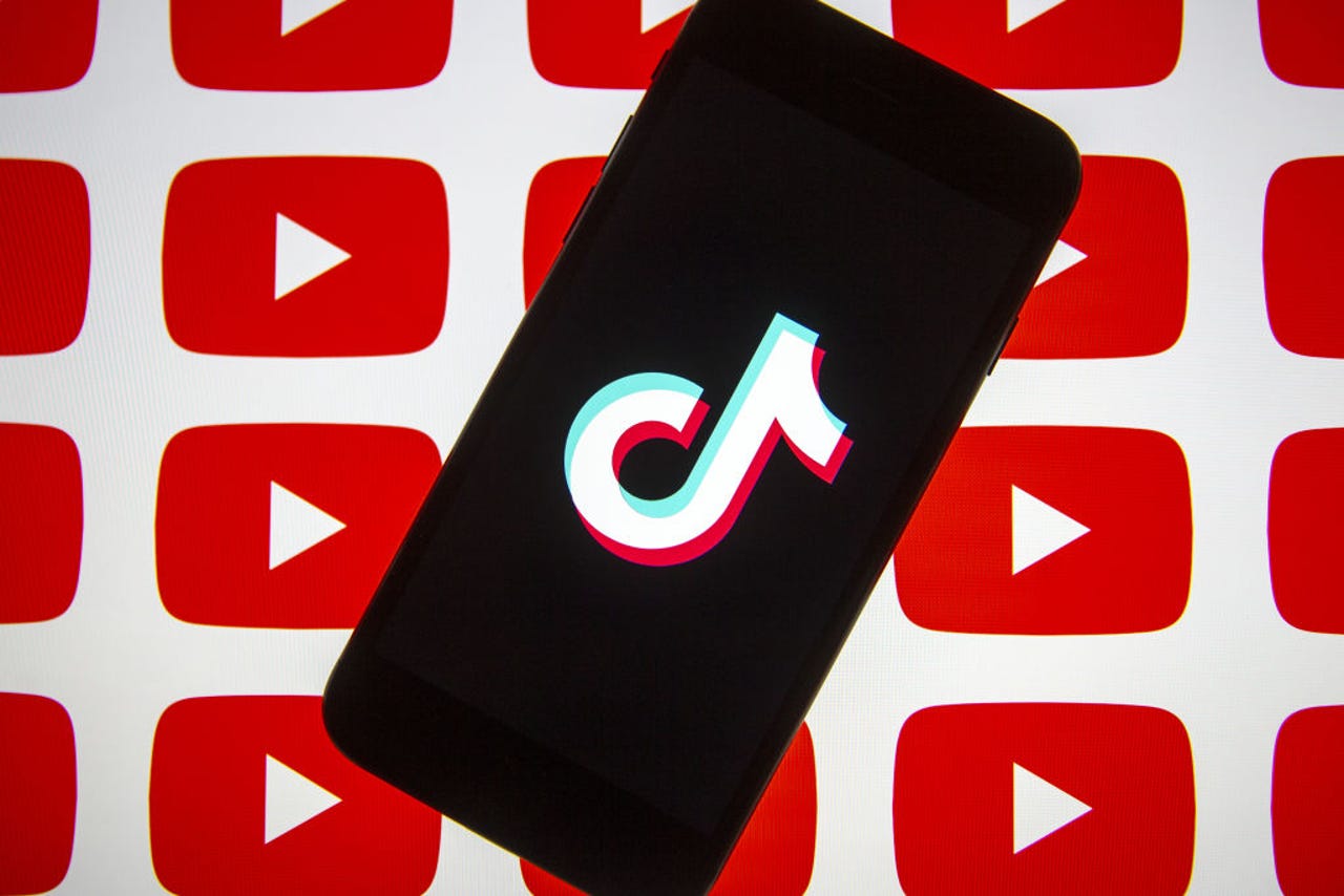 Ponsel menampilkan logo TikTok dengan latar belakang yang menampilkan logo youtube