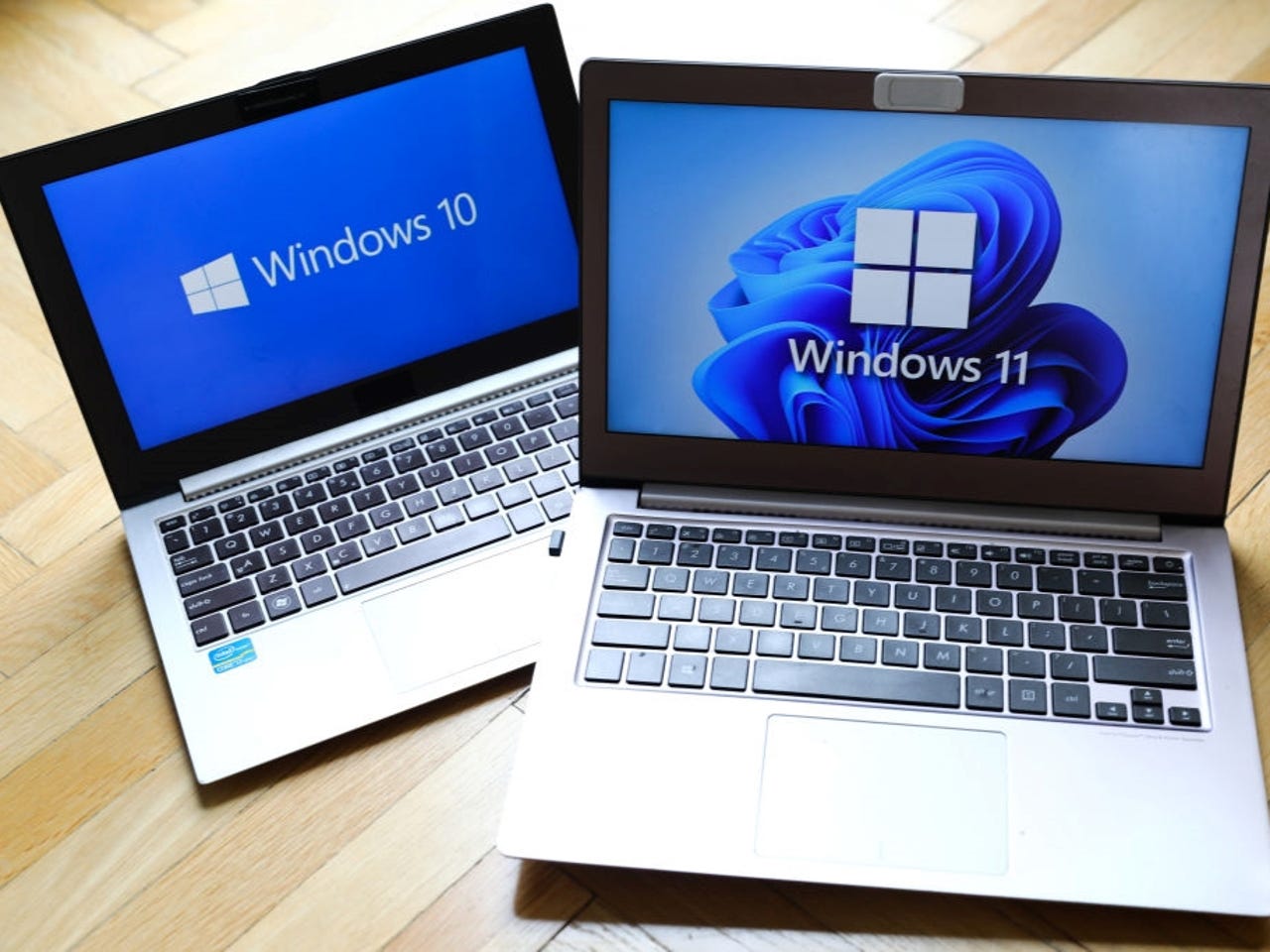 two laptop computers side by side, one displaying a blue background with a white windows 10 logo and the second with a patterned blue background displaying a windows 11 logo