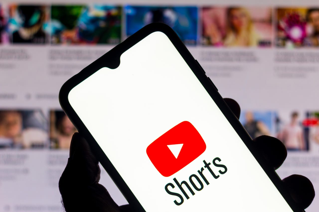 YouTube Shorts logo on a phone in front of a blurred background
