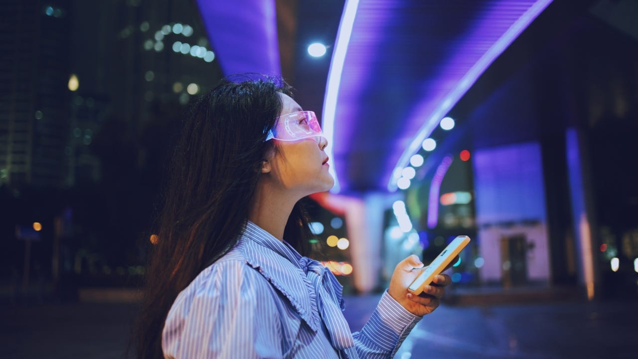 Young Asian woman using mobile phone while standing under a pedestrian bridge glowing at night