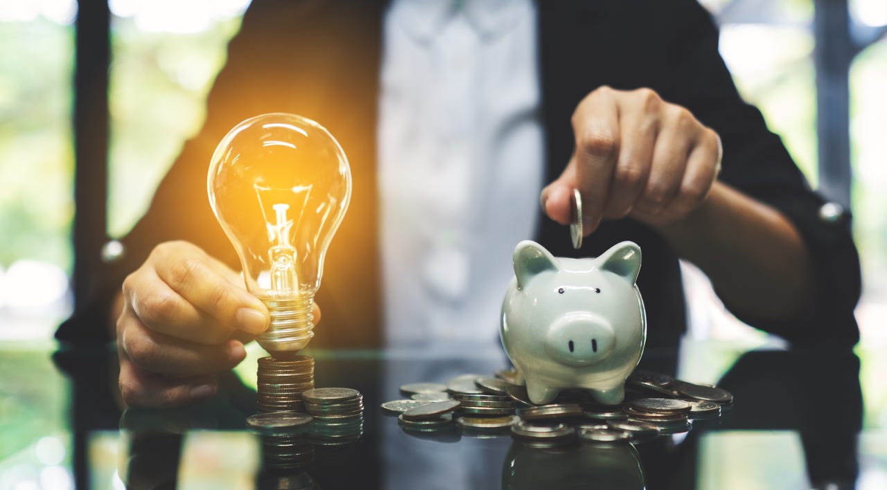 Person holding a lightbulb and piggy bank, saving money.