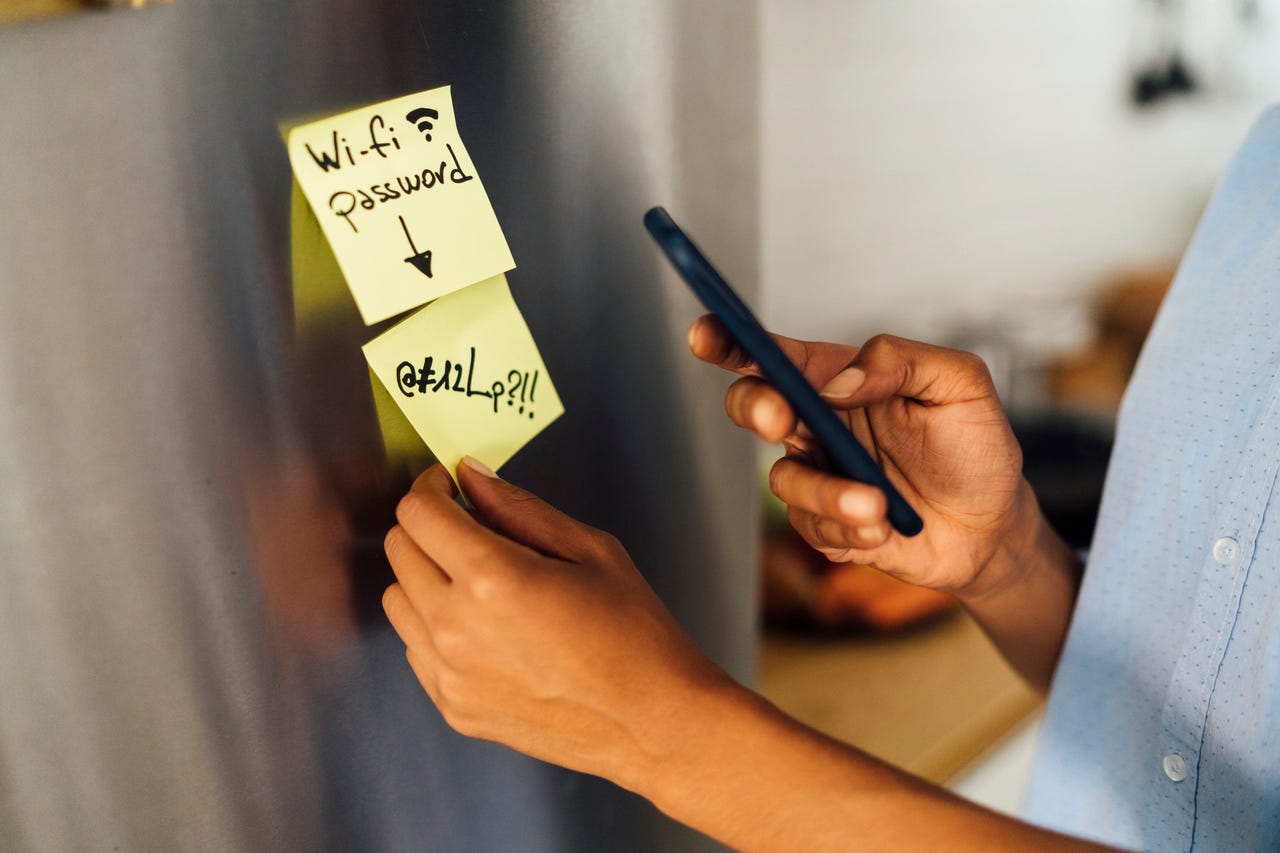 Woman in her kitchen checking password on sticky note on the fridge