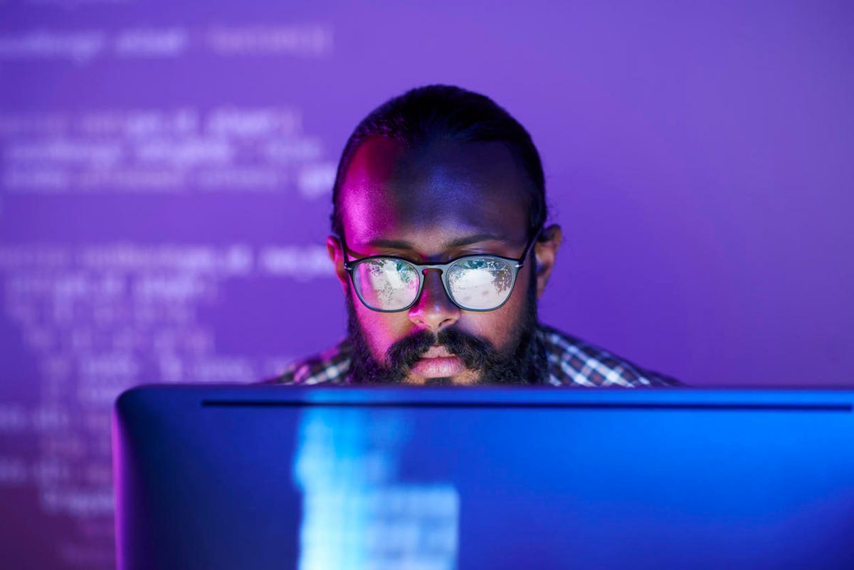 A serious young programmer wearing glasses focuses on working with encrypted data on a computer screen