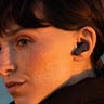 Close-up of a young woman at sunset using a pair of Skullcandy Dime 2 earbuds to listen to music.