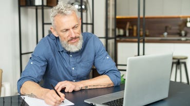 man with gray hair and beard writing notes in front of a computer