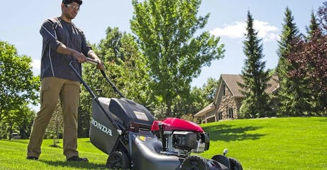 A man wearing a long-sleeved t-shirt and khaki pants using a Honda push mower on his lawn during a sunny day