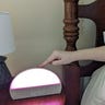 Person in bed pushing a button on a lit-up Hatch Restore 2 device on a nightstand