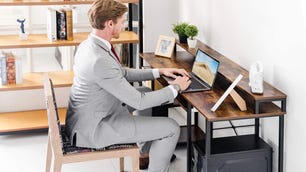 Man in suit sitting at a wooden desk typing on a laptop