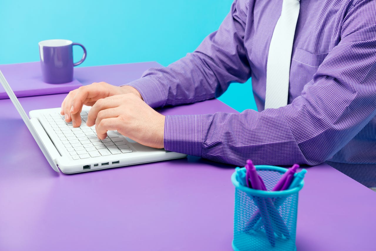 Businessman typing on laptop in office. Everything around is made of purple and blue colors.
