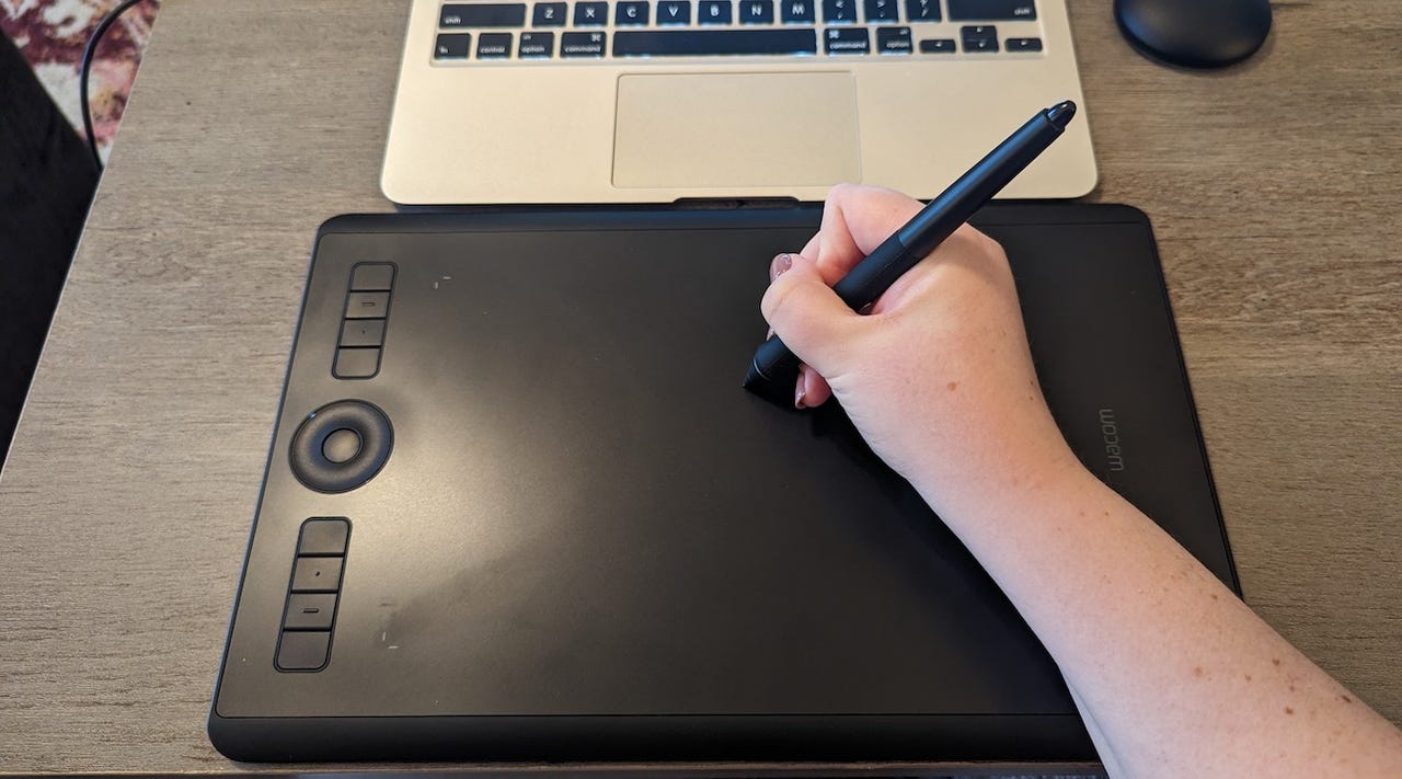Overhead image of person's hand holding a pen and writing on a black Wacom drawing tablet