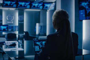 Female Special Agent Works on a Laptop in the Background Special Agent in Charge Talks To Military Man in Monitoring Room. In the Background Busy System Control Center with Monitors Showing Data Flow.