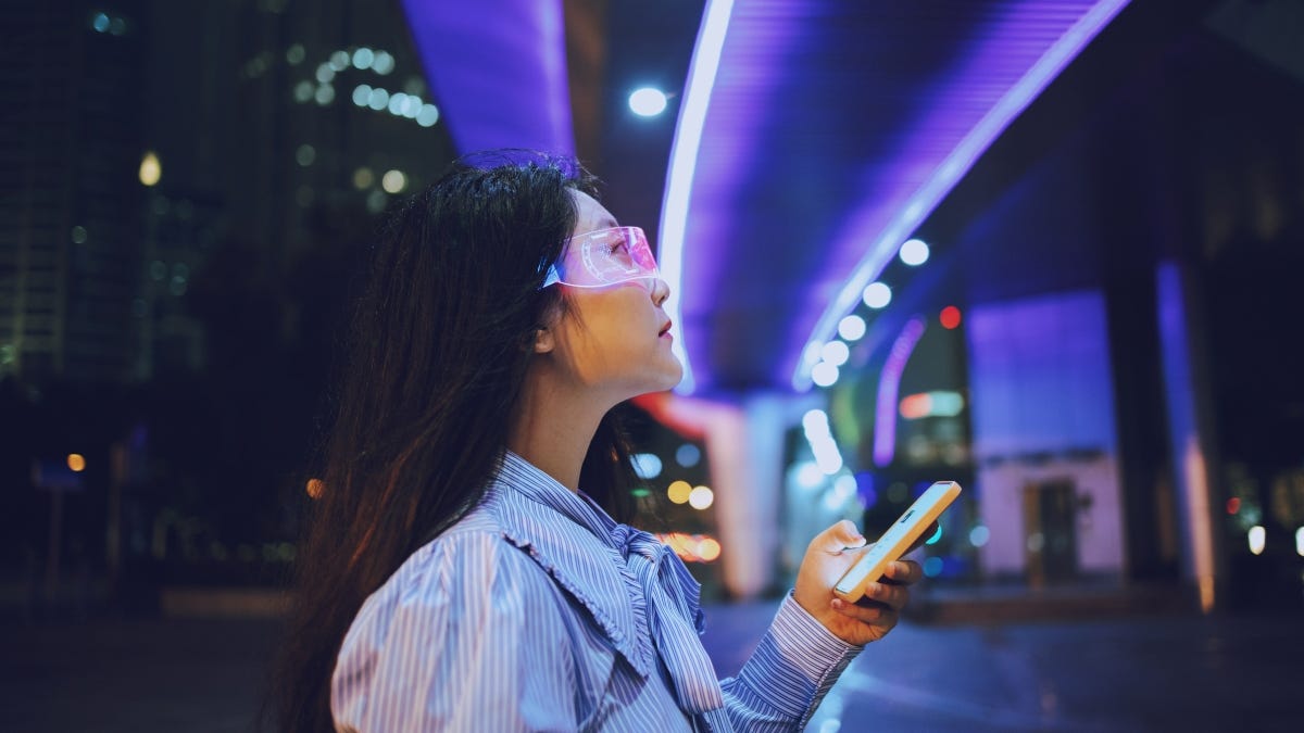 زن جوان آسیایی با استفاده از تلفن همراه در حالی که در زیر یک پل عابر پیاده که در شب می درخشد ایستاده است